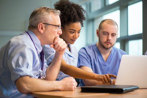 Three health professionals sitting at a desk, looking at a laptop screen.