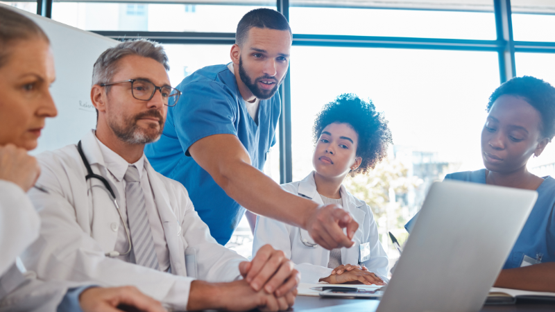 A group of health professionals sat together looking and pointing at a laptop screen.