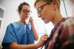 Female health professional using a stethoscope to listen to a patient's heart.