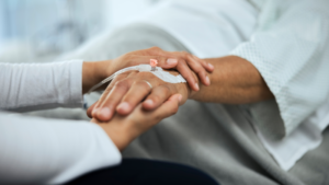 A health professional holding a patient's hand. The patient has a Intravenous cannula in their hand.