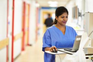 Health professional standing in ward using computer.
