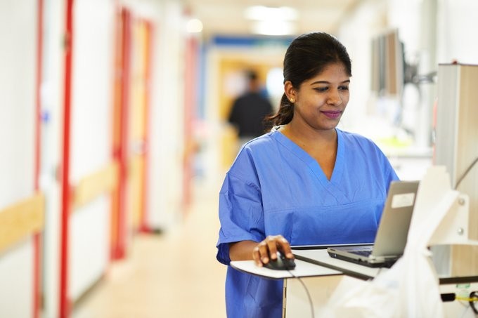 Health professional standing in ward using computer.